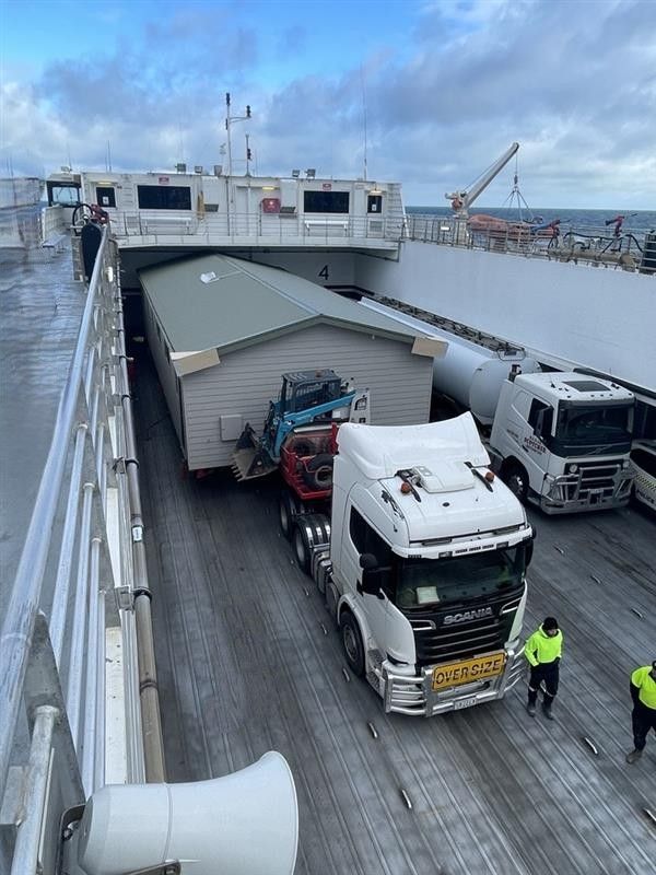 Trucks on a ferry’s car deck with a partially collapsed trailer roof and workers nearby