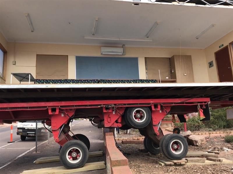 Red truck chassis tilted on a ramp outside a building with a garage-style doorway