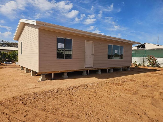 Small beige house on stilts in a sandy construction area under a blue sky