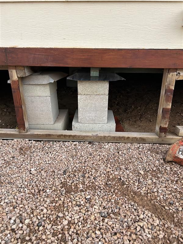House foundation on cinder blocks above gravel, showing crawl space beneath the wall