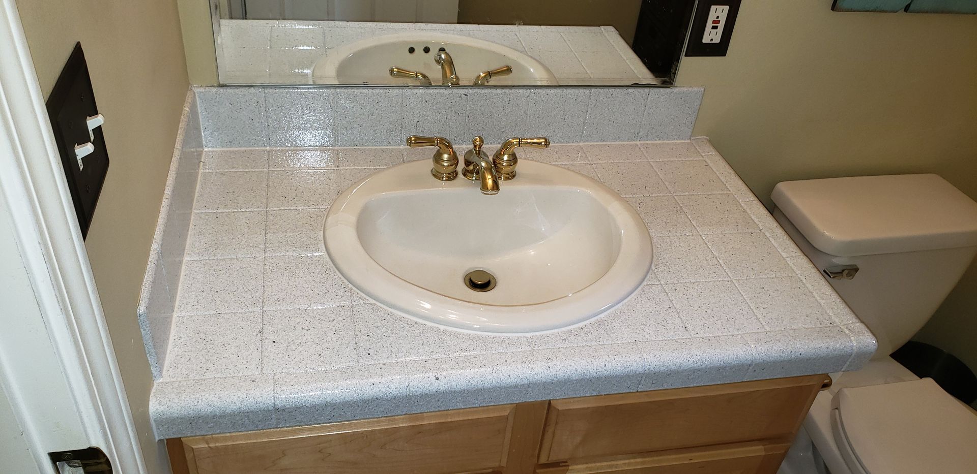 Bathroom sink with a white speckled countertop and wood cabinets. A toilet is visible on the right.