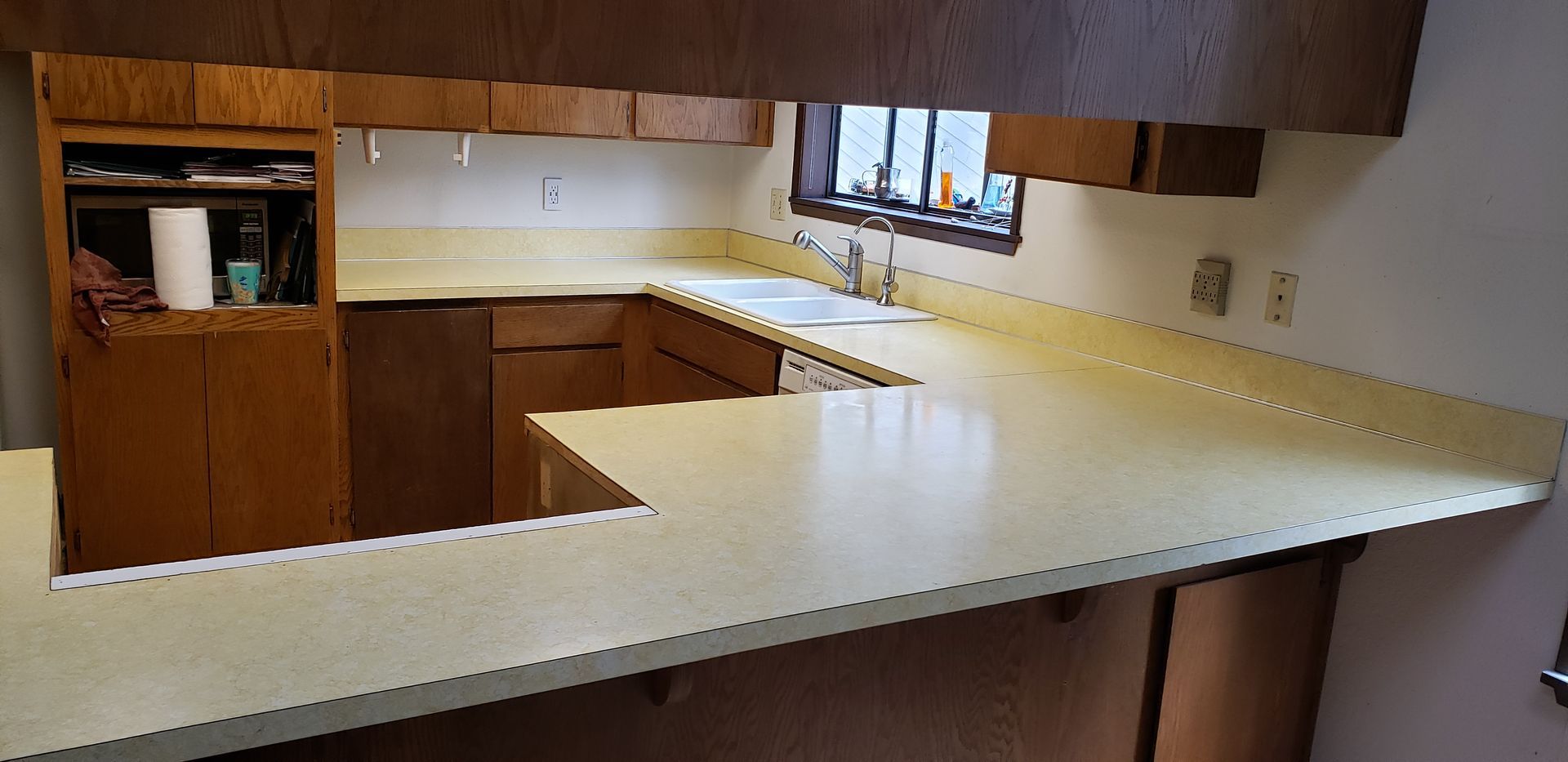A kitchen with brown cabinetry, yellow countertops, and a pass-through to a dining area.