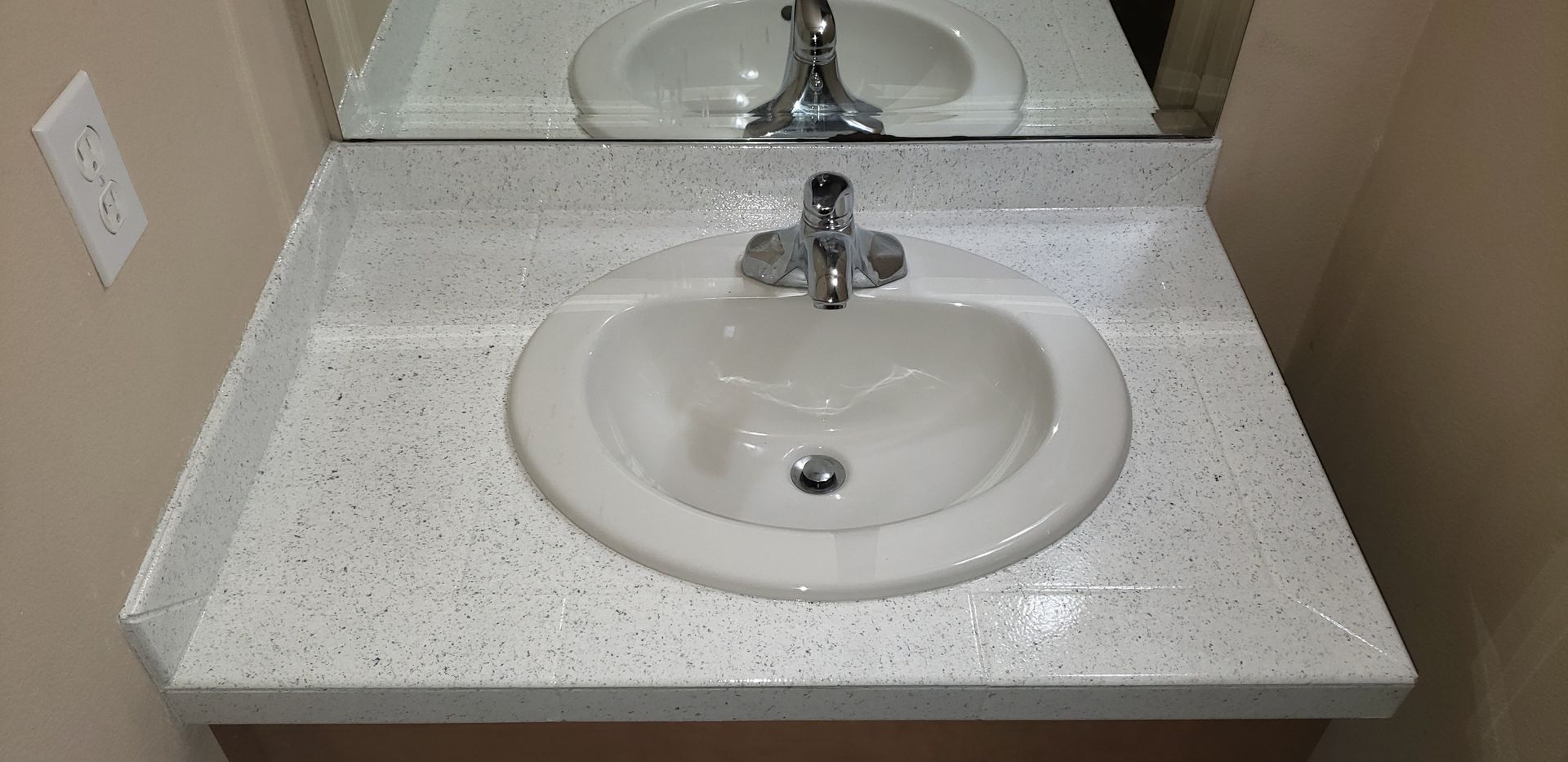White bathroom sink with speckled countertop, faucet, and mirror reflection.