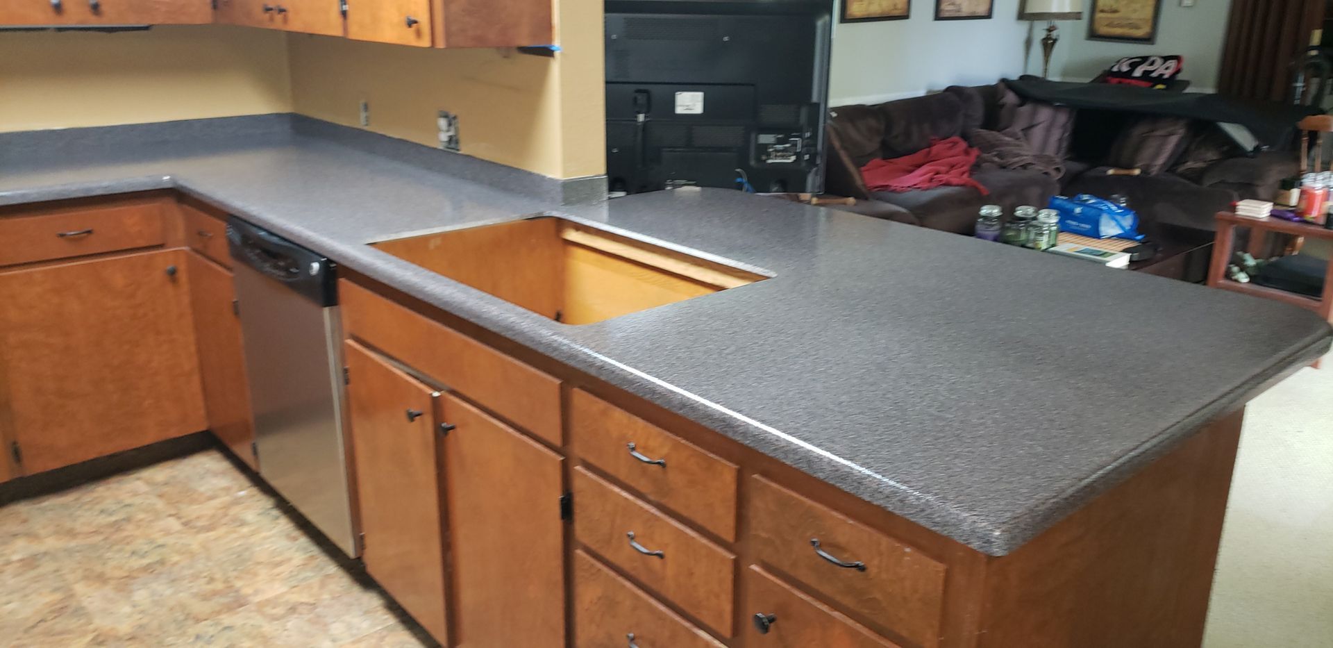 Kitchen with brown cabinets, dark countertops, a dishwasher, and an empty sink space.