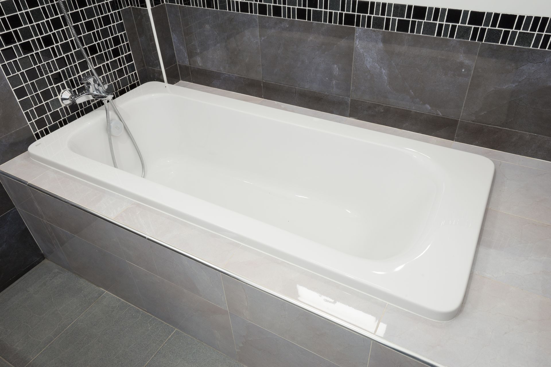 Clean white bathtub surrounded by modern gray and black tile. 