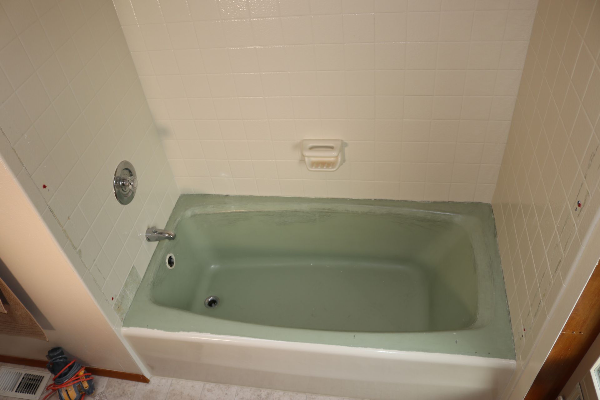 Green bathtub in white-tiled bathroom. Silver faucet and soap dish.
