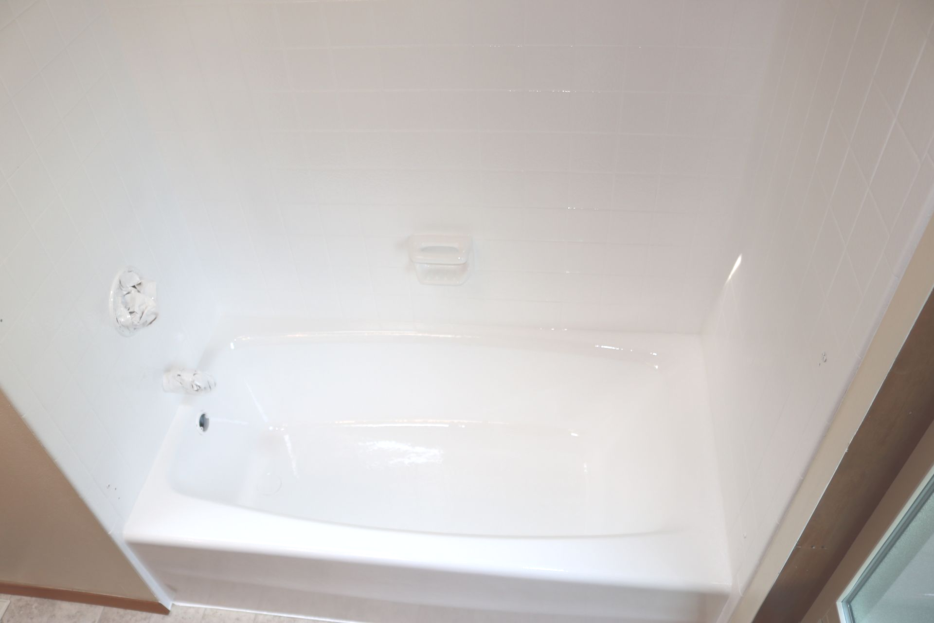 White bathtub inside a shower with white walls, soap dish, and faucet.