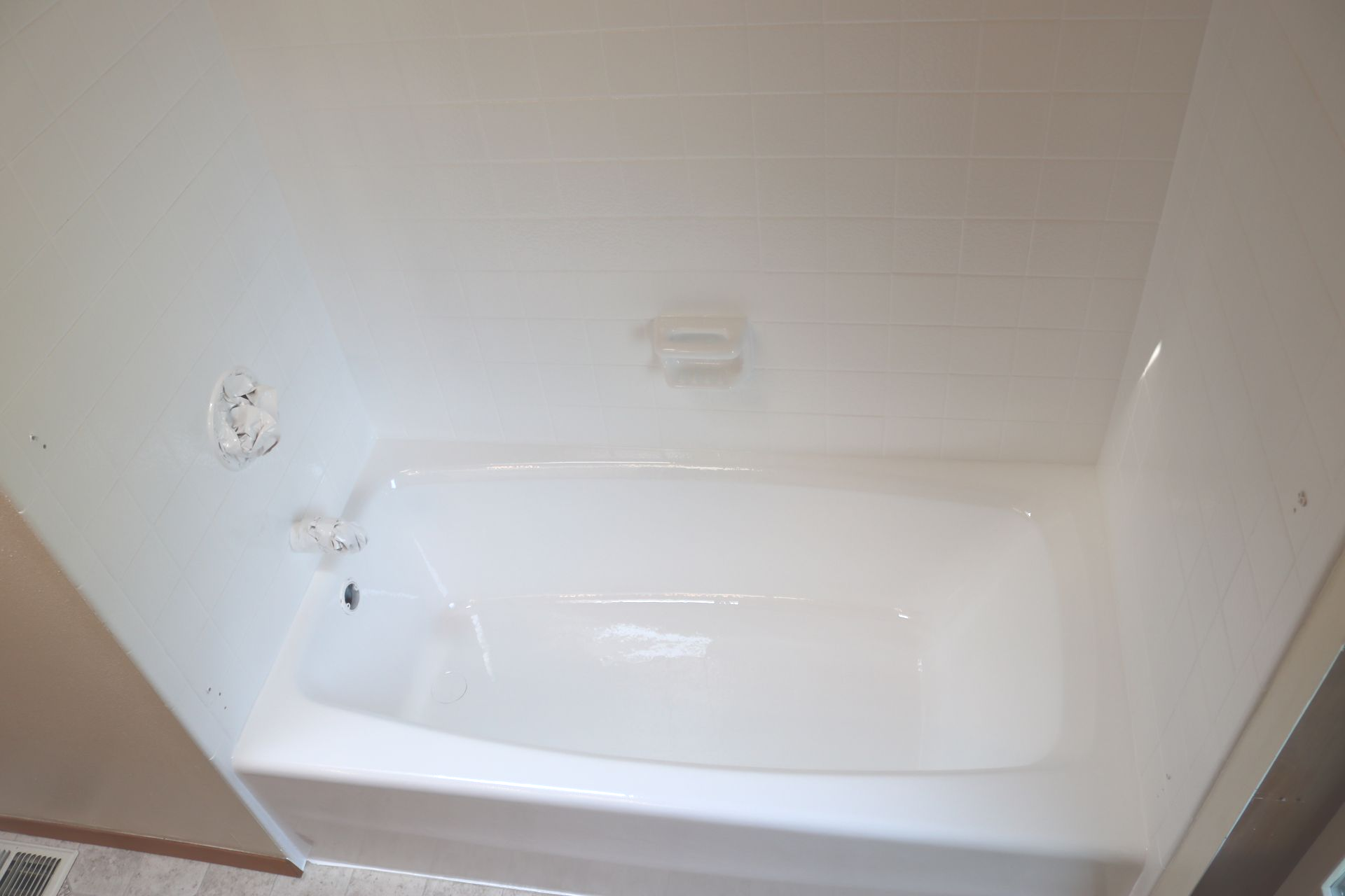 White bathtub inside a white-walled shower enclosure. A soap dish is mounted on the wall.