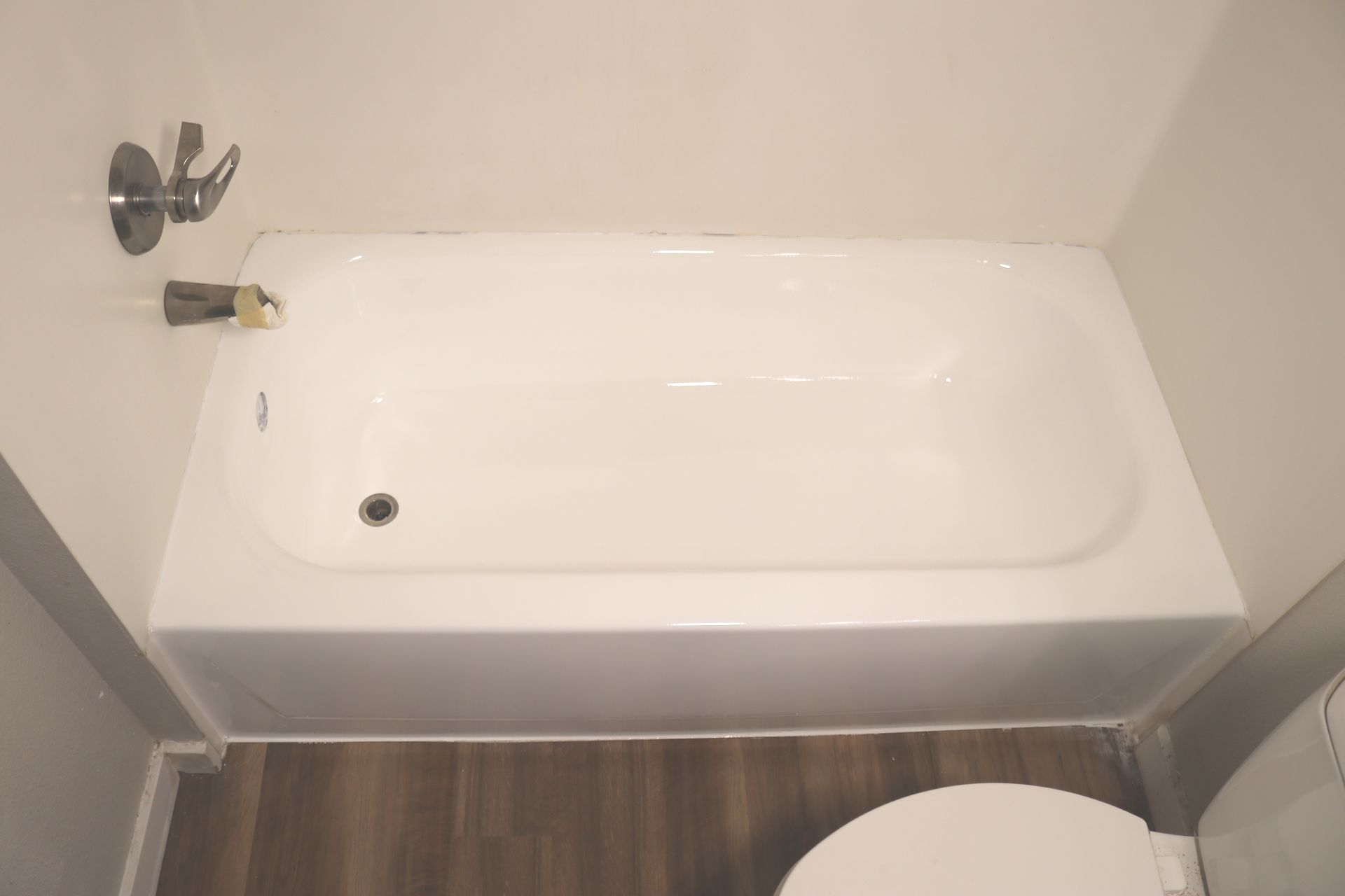 White bathtub in a bathroom, with a faucet on the wall and a toilet on the floor.