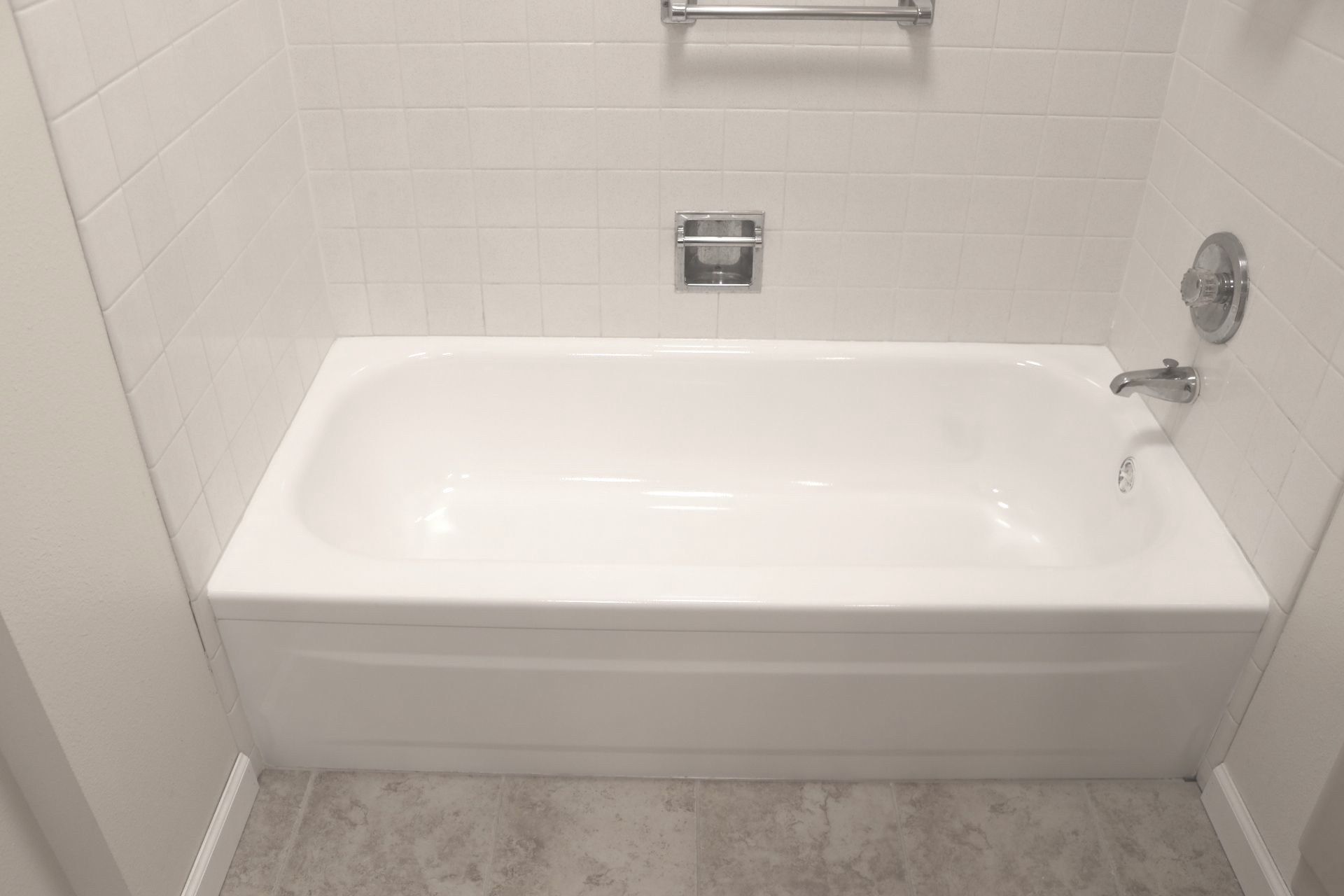 White bathtub in a tiled alcove with silver fixtures.