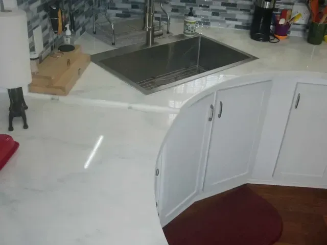 White kitchen countertop with sink, cabinets, and dark red floor mat.