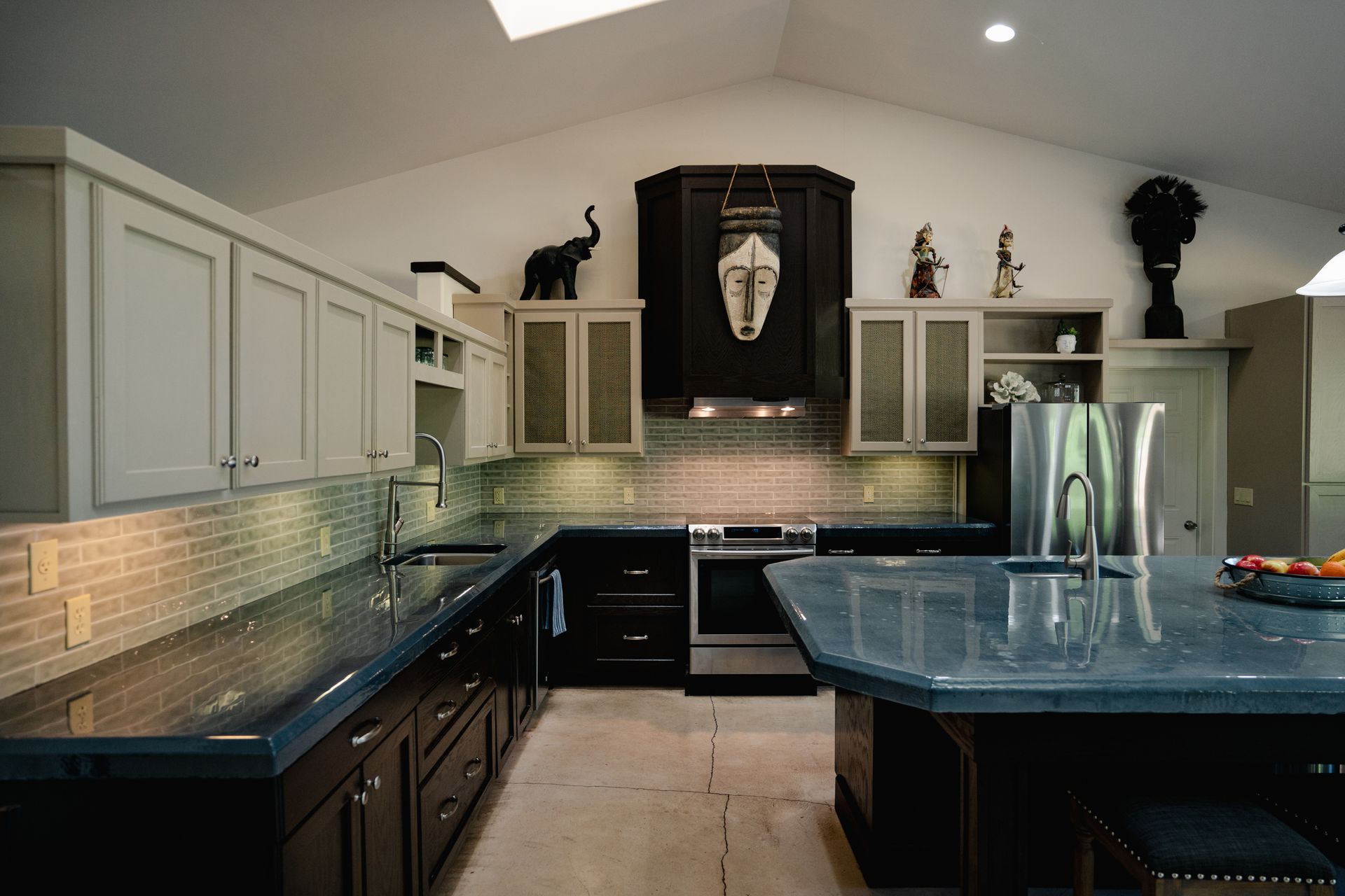 U-shaped kitchen with dark countertops, white cabinets, and African art decor.