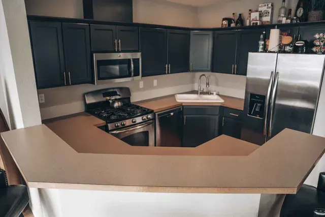 Kitchen with dark cabinets, stainless steel appliances, tan countertops, and a bar.