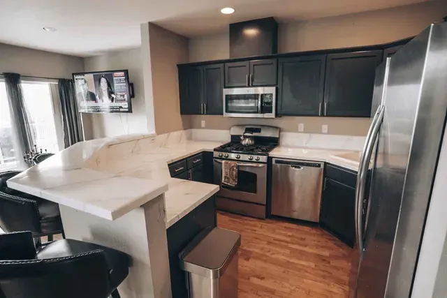 Modern kitchen with dark cabinets, stainless steel appliances, and a white countertop with bar seating.