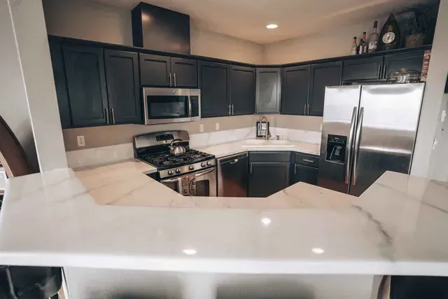 Modern kitchen with dark cabinets, stainless steel appliances, and white marble countertops.