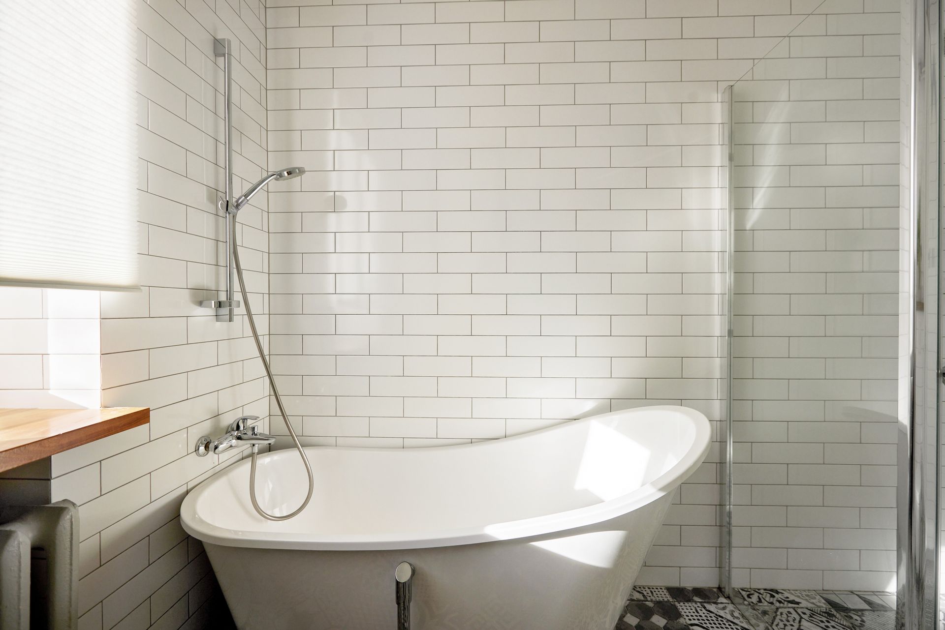 Modern bathroom with white tiles, freestanding tub, and handheld showerhead.