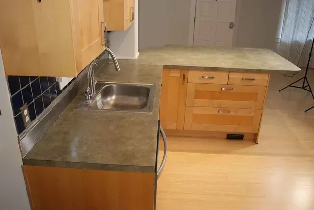 Kitchen with light wood cabinets, gray countertop, stainless steel sink, and island.