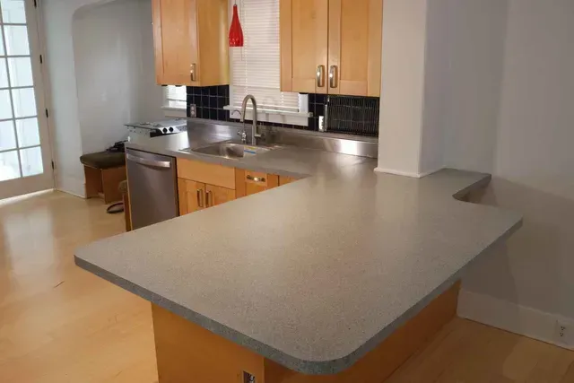 A kitchen with light wood cabinets, gray countertops, and a stainless steel sink.