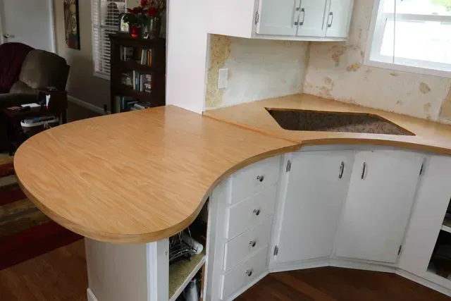Light wood countertop curves around white cabinets, open shelving, and kitchen window.