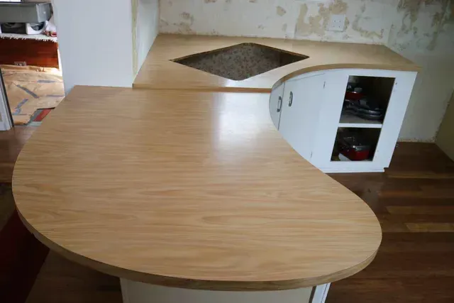 Light wood-toned kitchen island with curved end. Built-in cabinets and countertops.