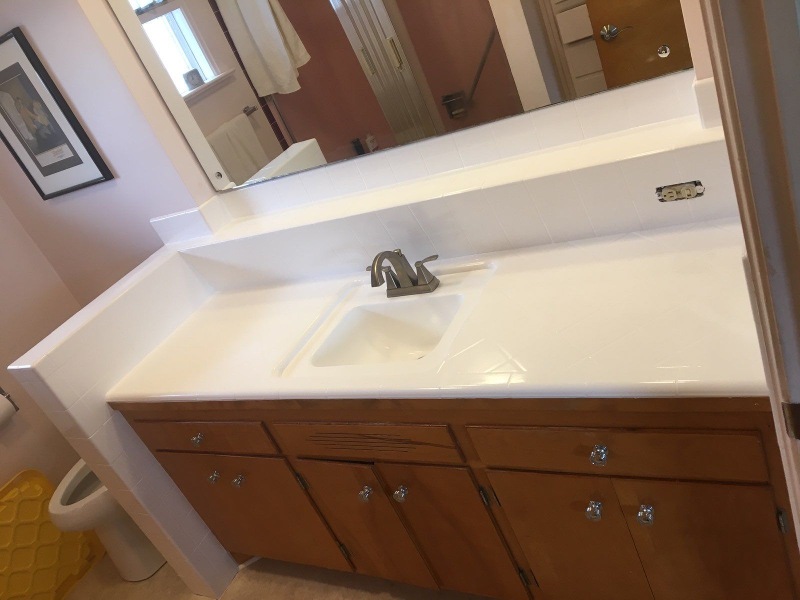 Bathroom with white sink, brown cabinets, and a framed picture.