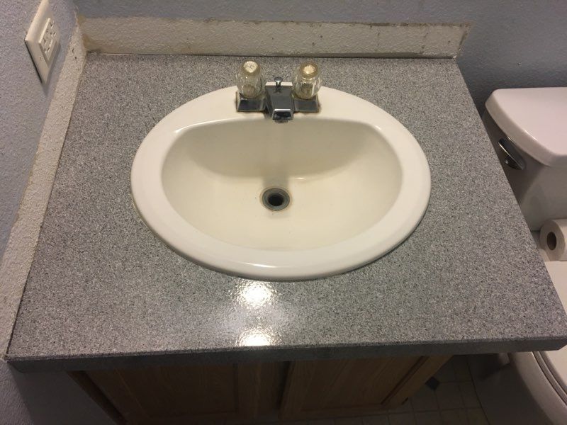 White oval sink in a speckled gray countertop with a chrome faucet. Wooden cabinet below.
