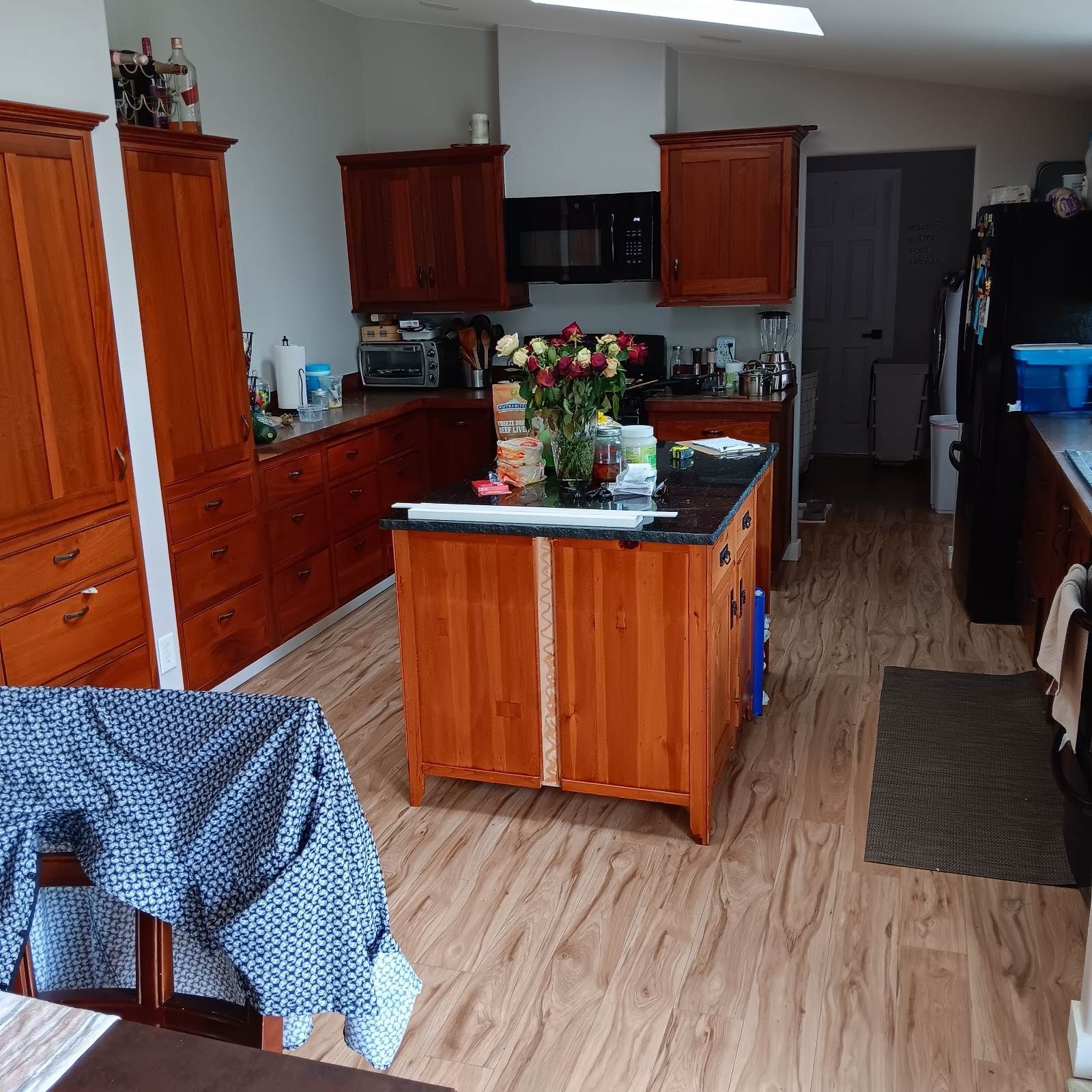 Kitchen with cherry-stained cabinets, island, and wood-look flooring. A black microwave and refrigerator are visible.