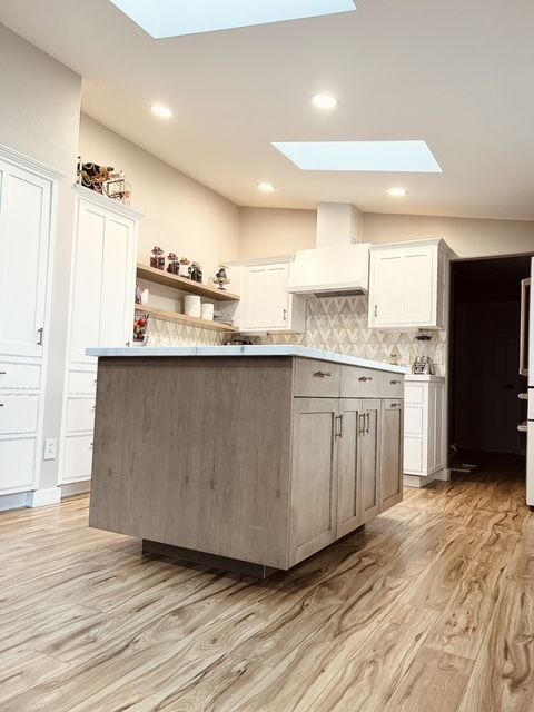 Modern kitchen with light wood floors, large island, white cabinets, and skylights.