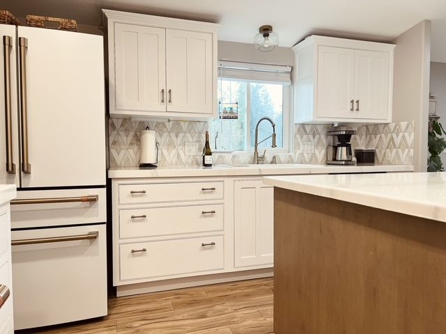 White kitchen with gold hardware. White cabinets, backsplash, and island countertop. Light brown island base and flooring.
