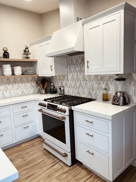 White kitchen with white cabinets, stove, range hood, and geometric backsplash.
