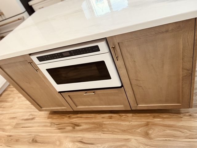 Built-in microwave in a light wood kitchen island with a white countertop and wooden floor.