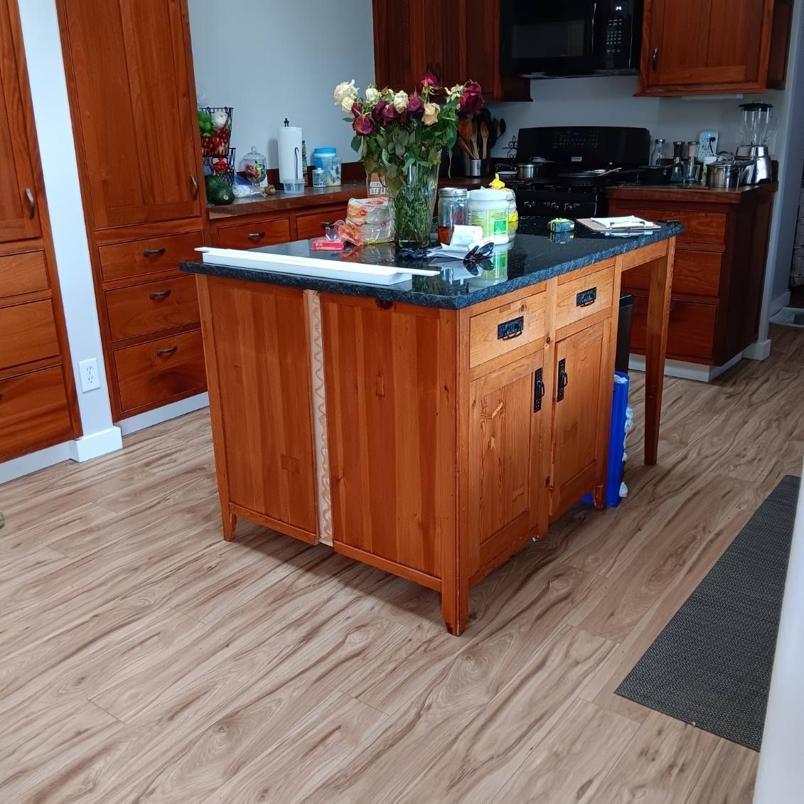 Kitchen with wooden cabinets and island, hardwood floors. Flowers on the island, black countertops.