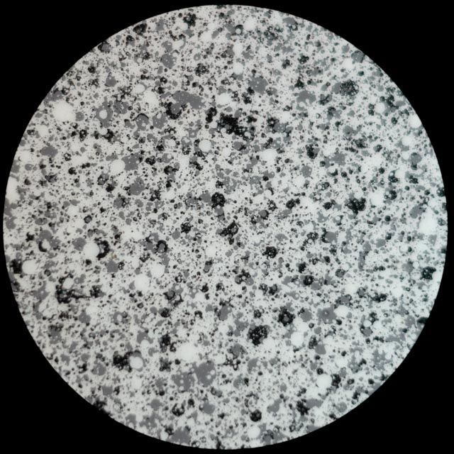 Speckled pattern of gray, black, and white dots, resembling granite, within a circular frame.