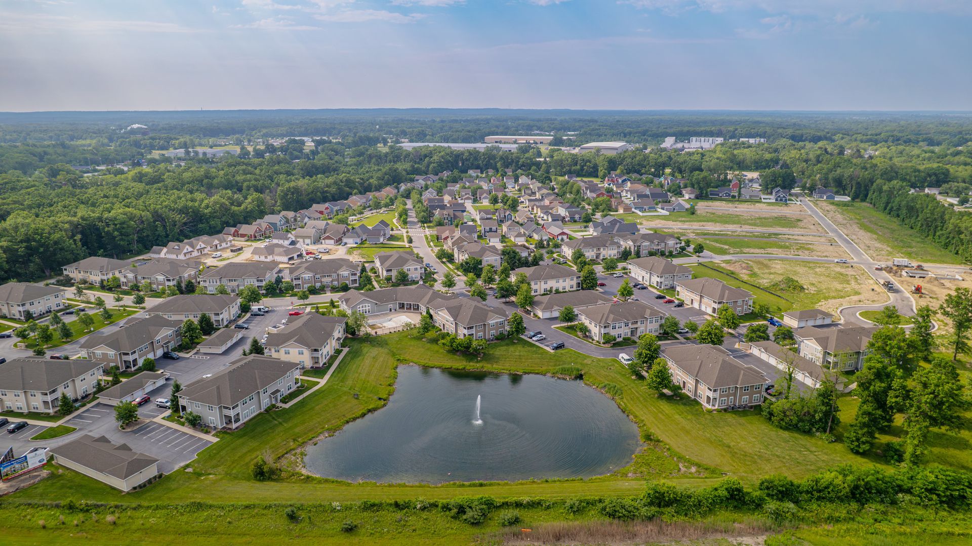 Aerial view of a suburban neighborhood with a pond in front of houses and trees.