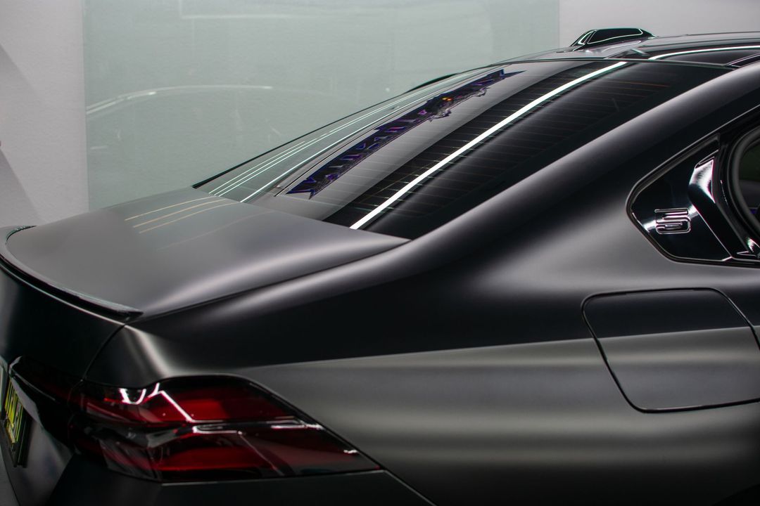 Black sports sedan rear corner in a garage, showing taillights and glossy body lines