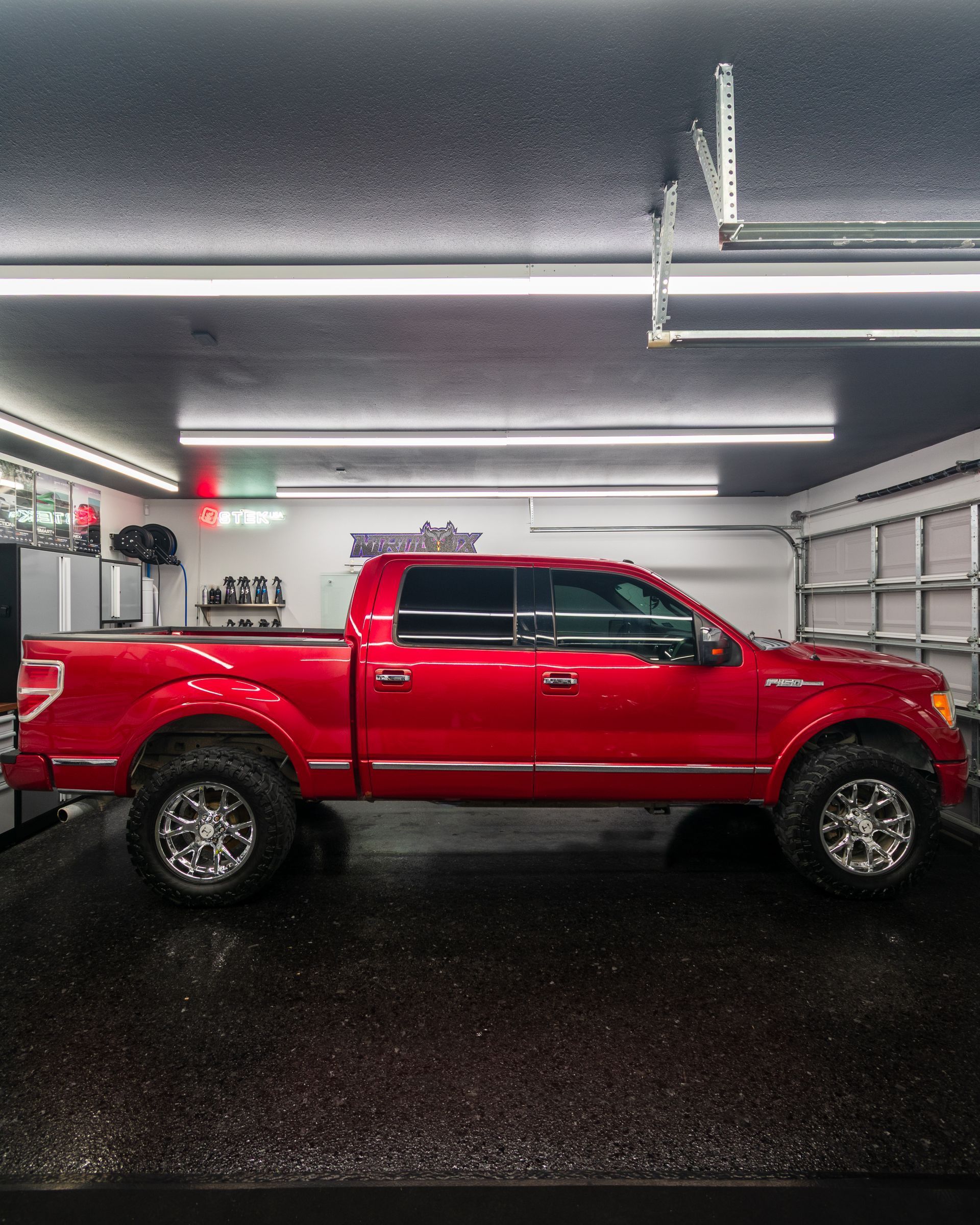 Red lifted pickup truck parked inside a garage, viewed from the side.