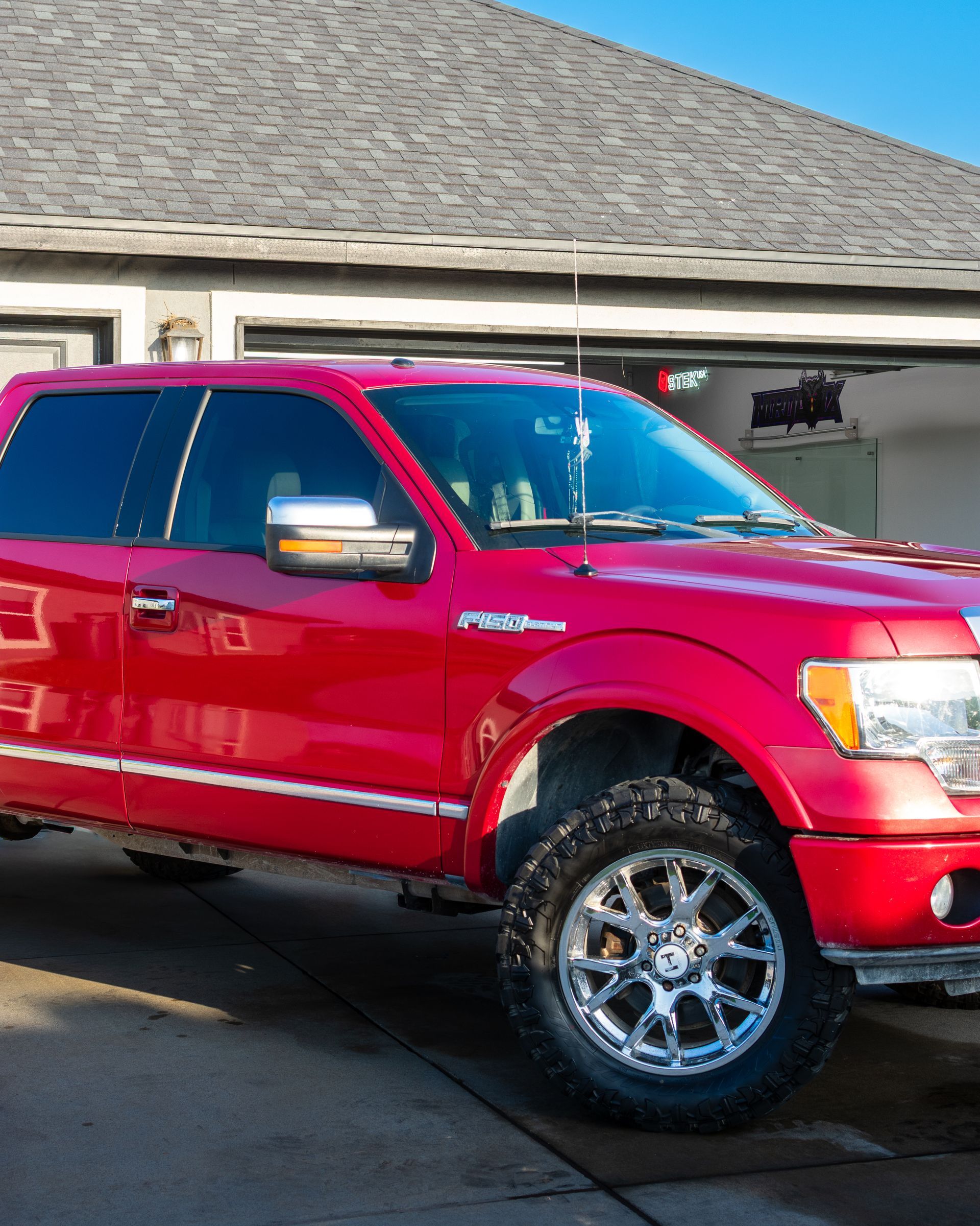 Red lifted pickup truck parked in front of a garage on a sunny driveway