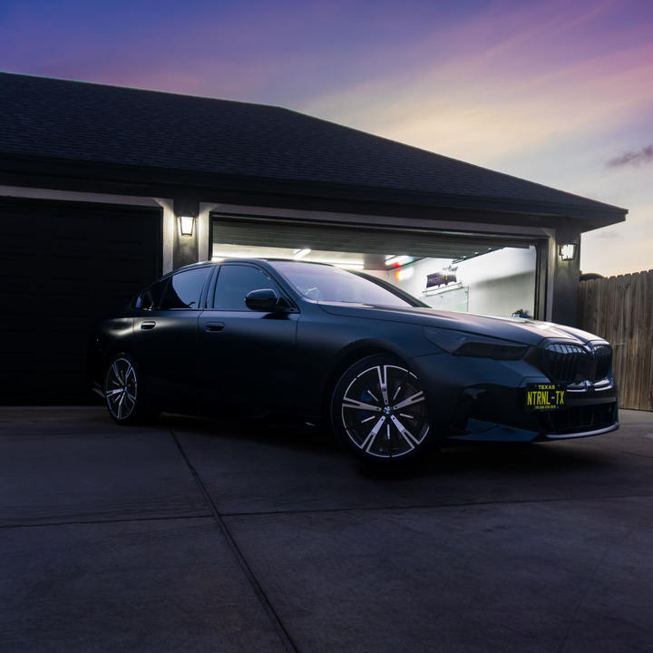 Black sedan parked in a driveway at dusk beside a lit garage.