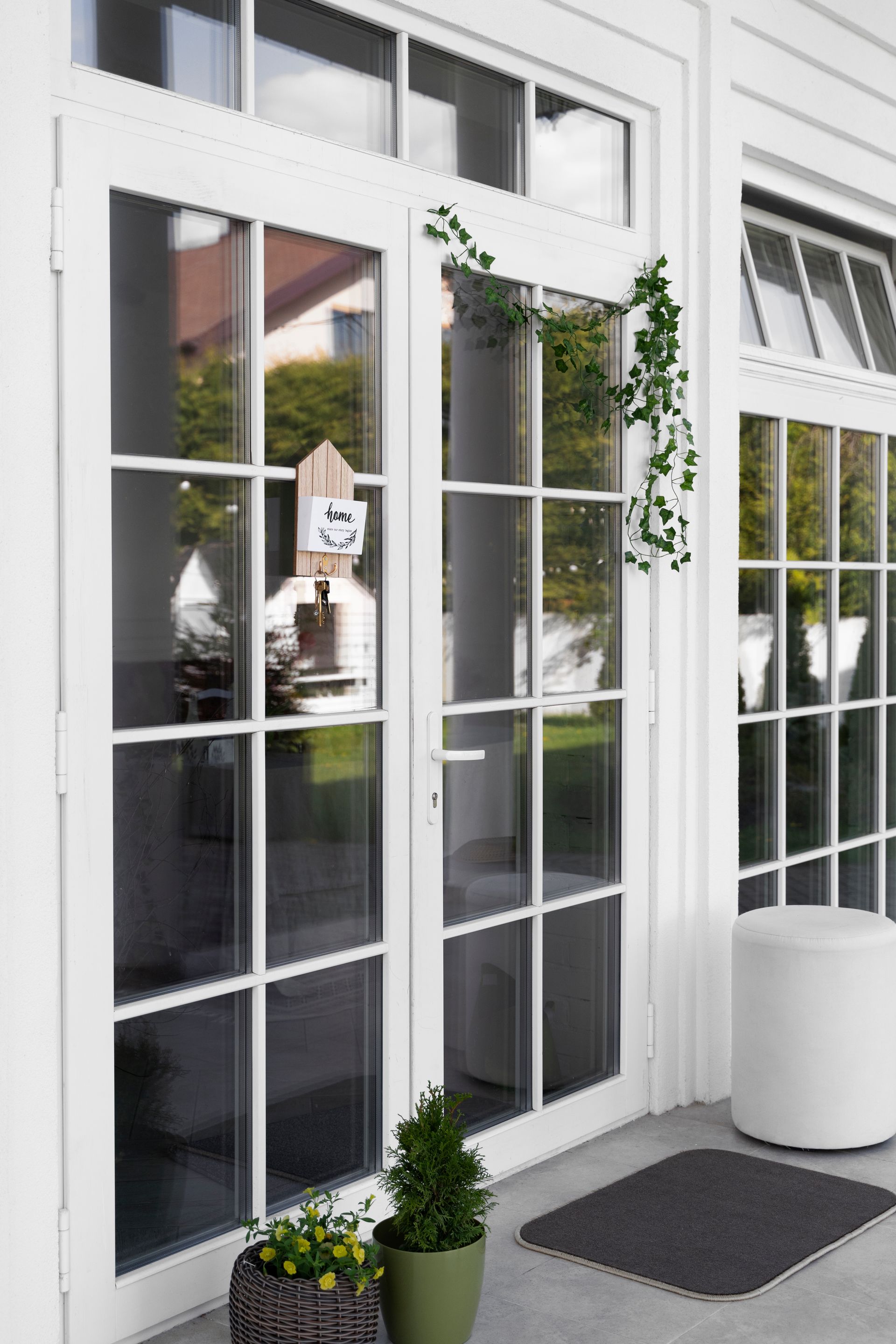 White French doors with glass panes beside a patio, with potted plants and a dark doormat.