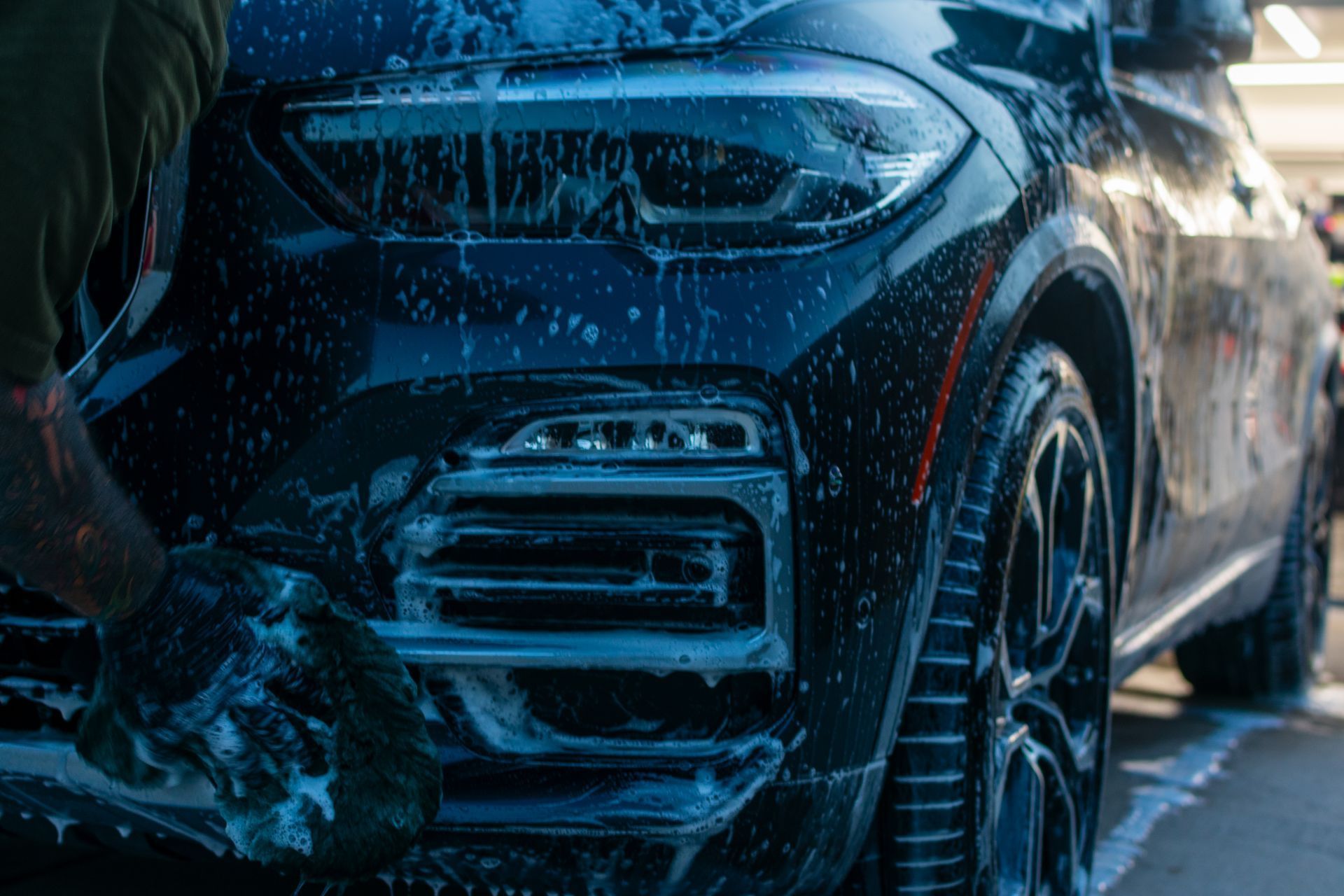 Close-up of a dark blue SUV with snow and water on the front bumper and wheel in winter conditions