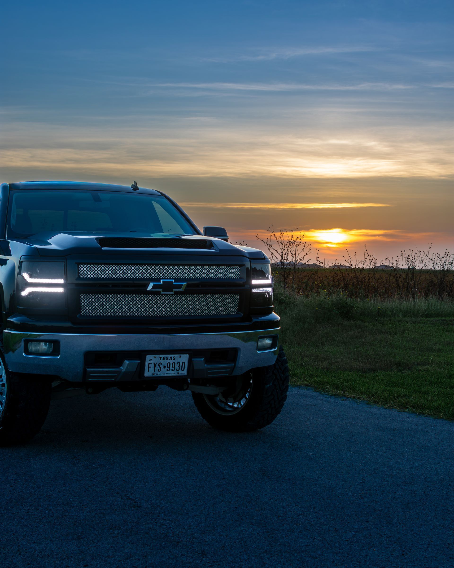 Black pickup truck parked by a road at sunset with the sun over a marshy horizon.