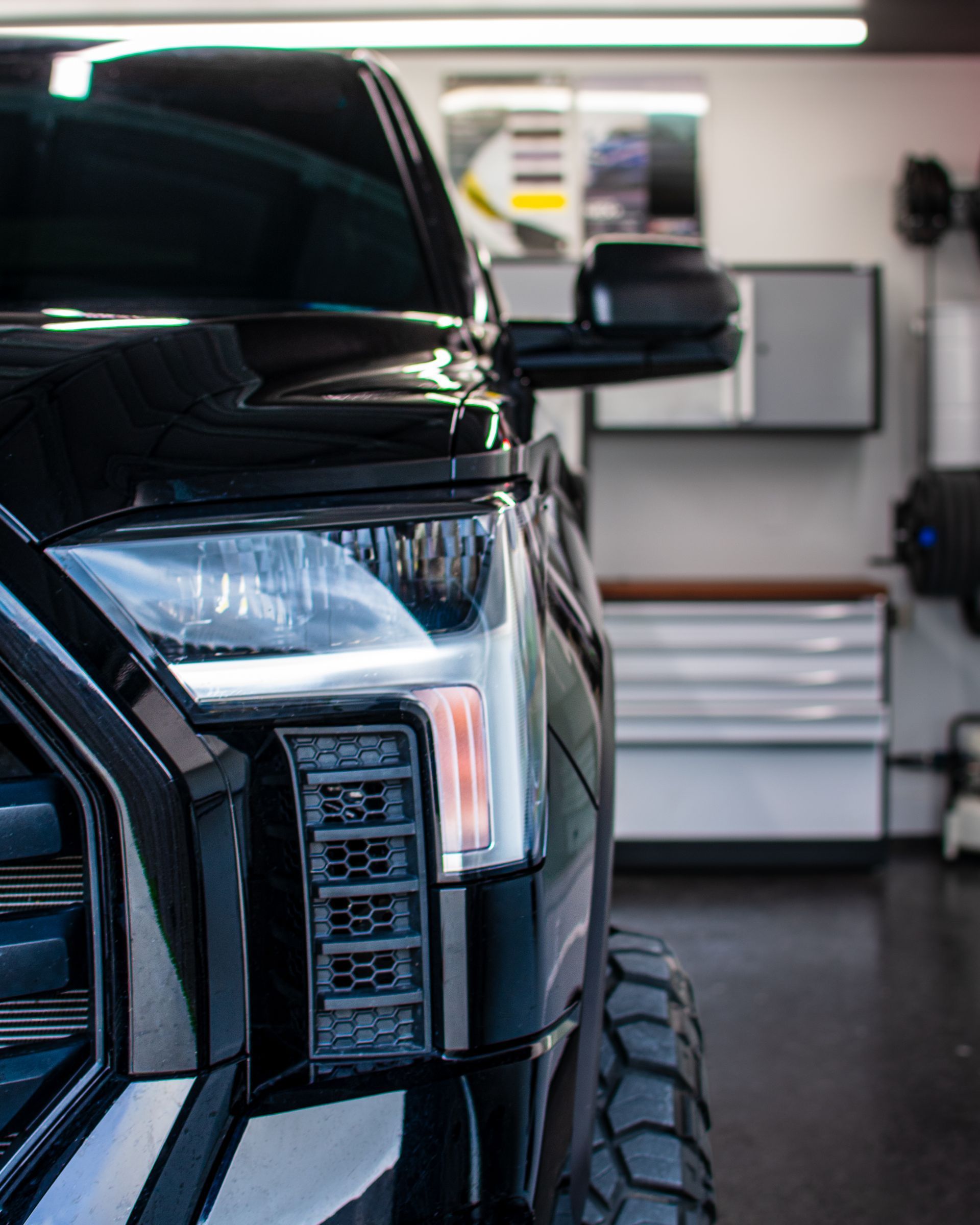 Black pickup truck front in a garage, showing headlight and tire detail.