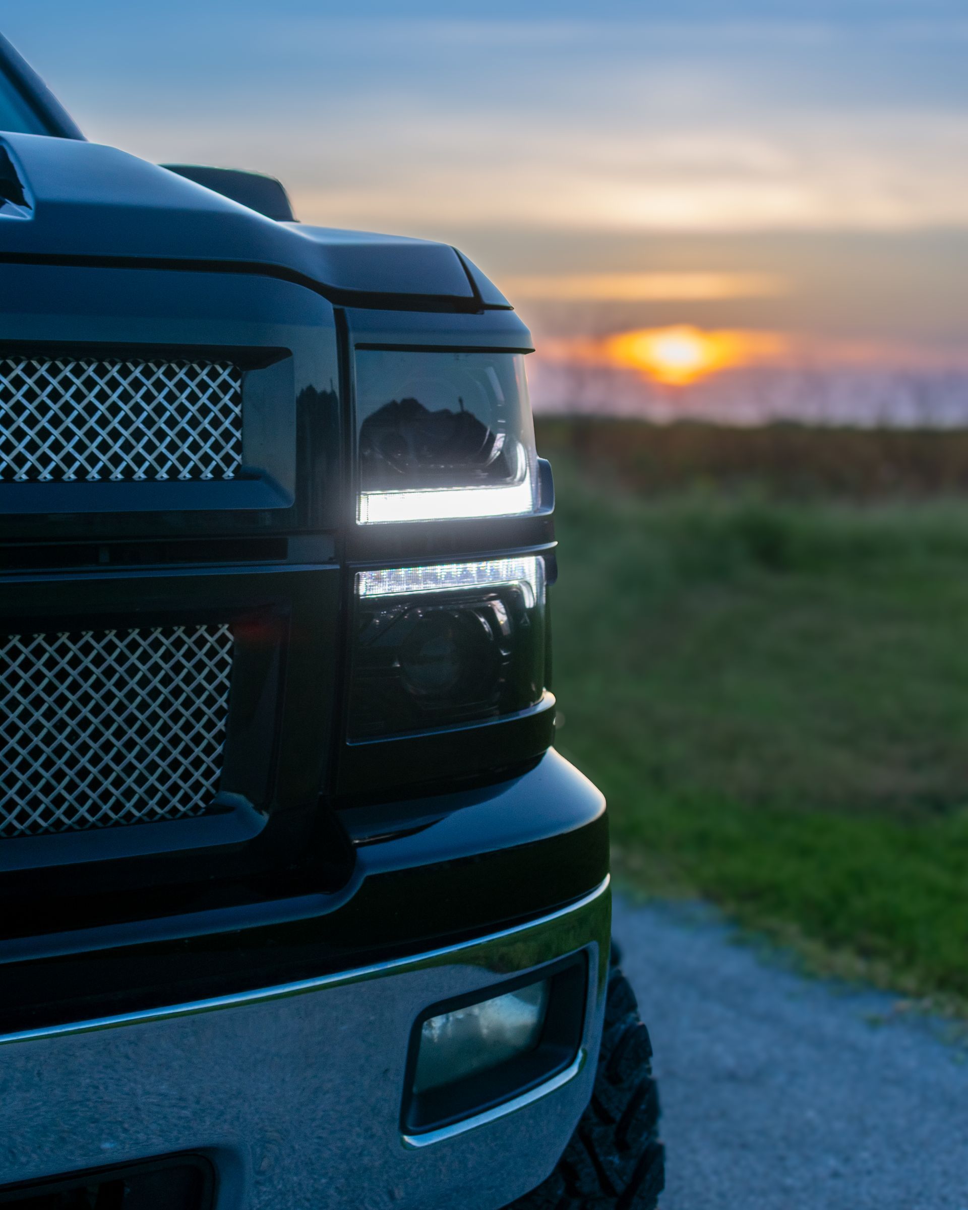 Black pickup truck front end on a rural road at sunset