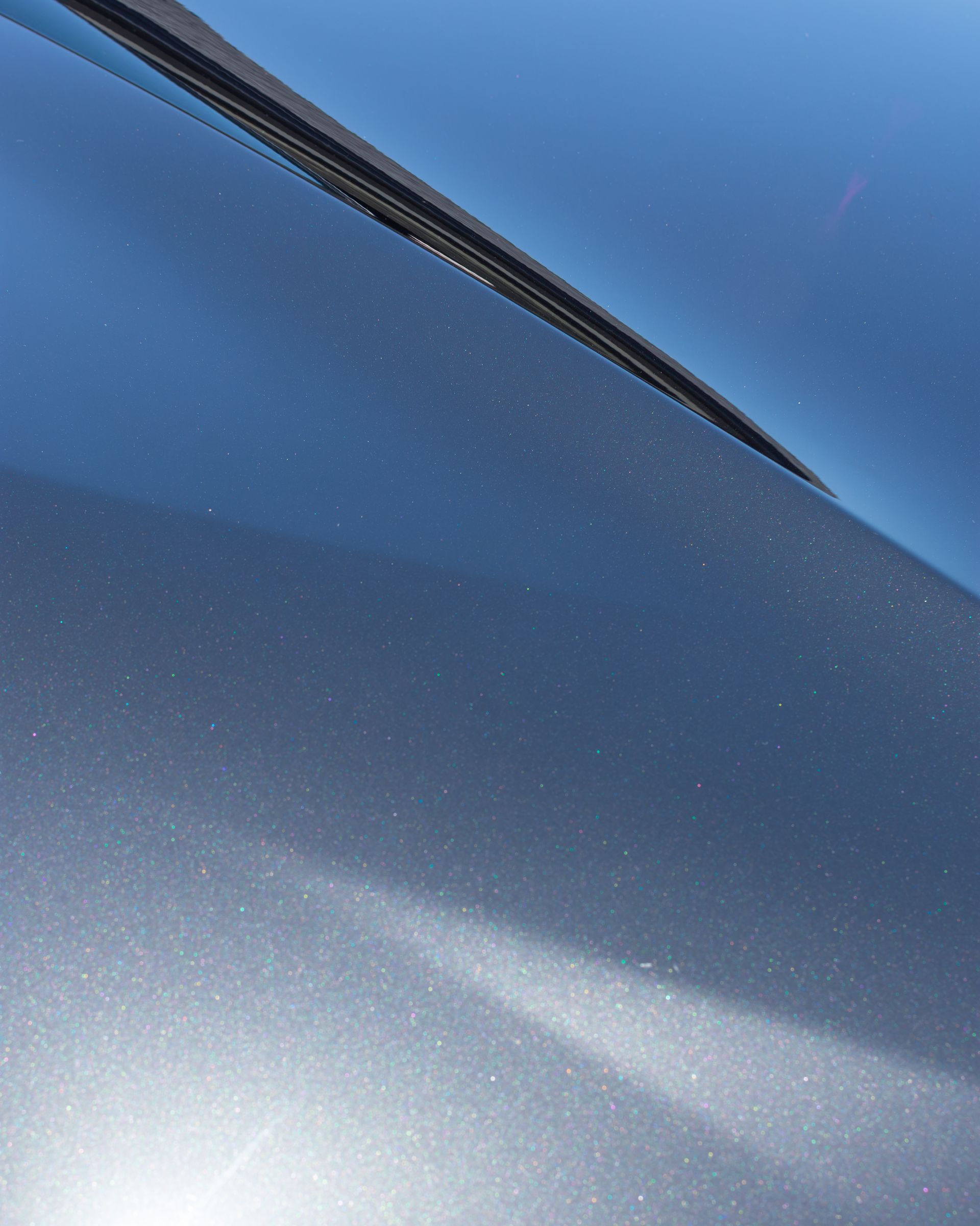 Close-up of blue metallic car body with a windshield edge and light reflection