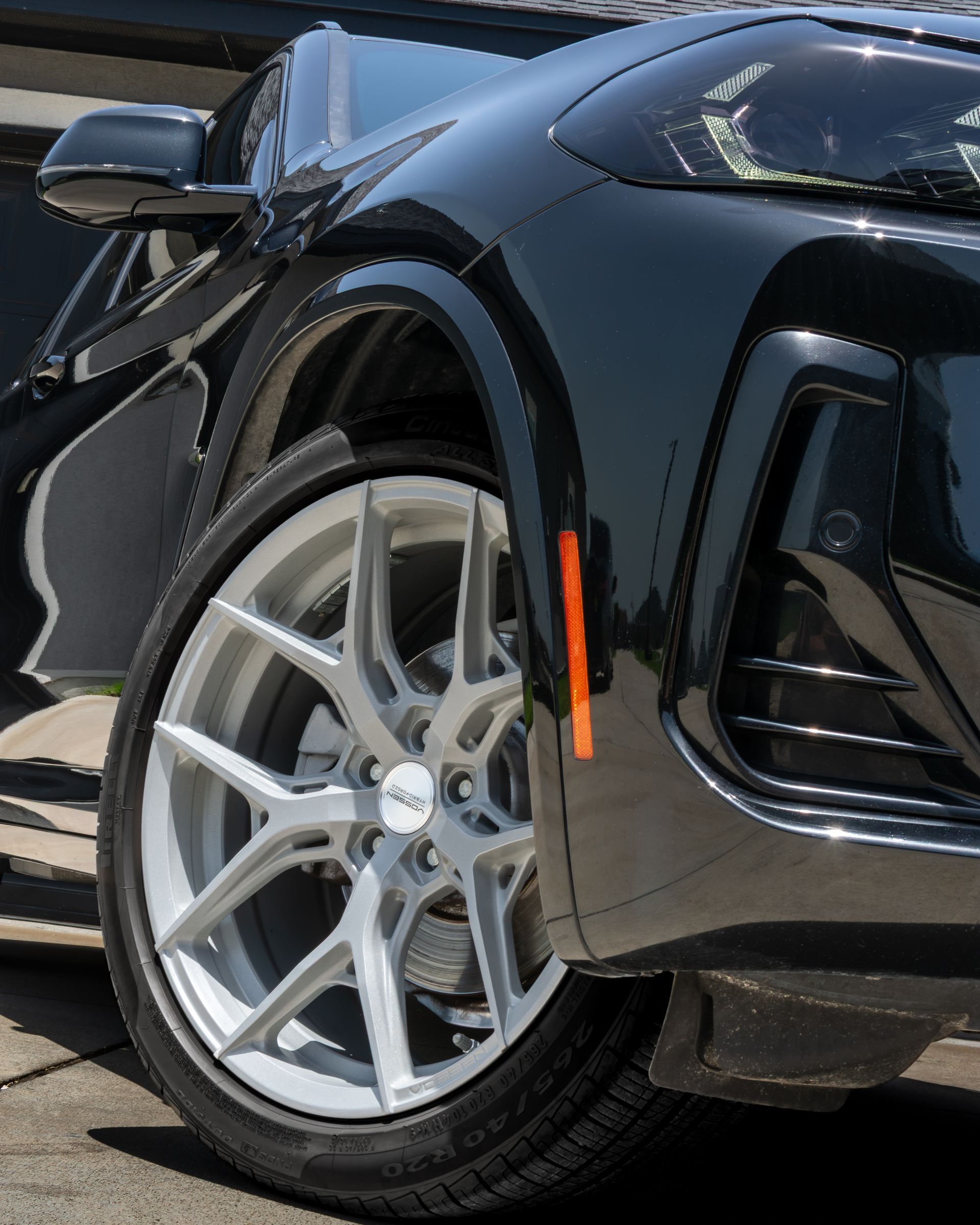 Close-up of a black car’s front wheel and fender with silver alloy rim and orange side marker