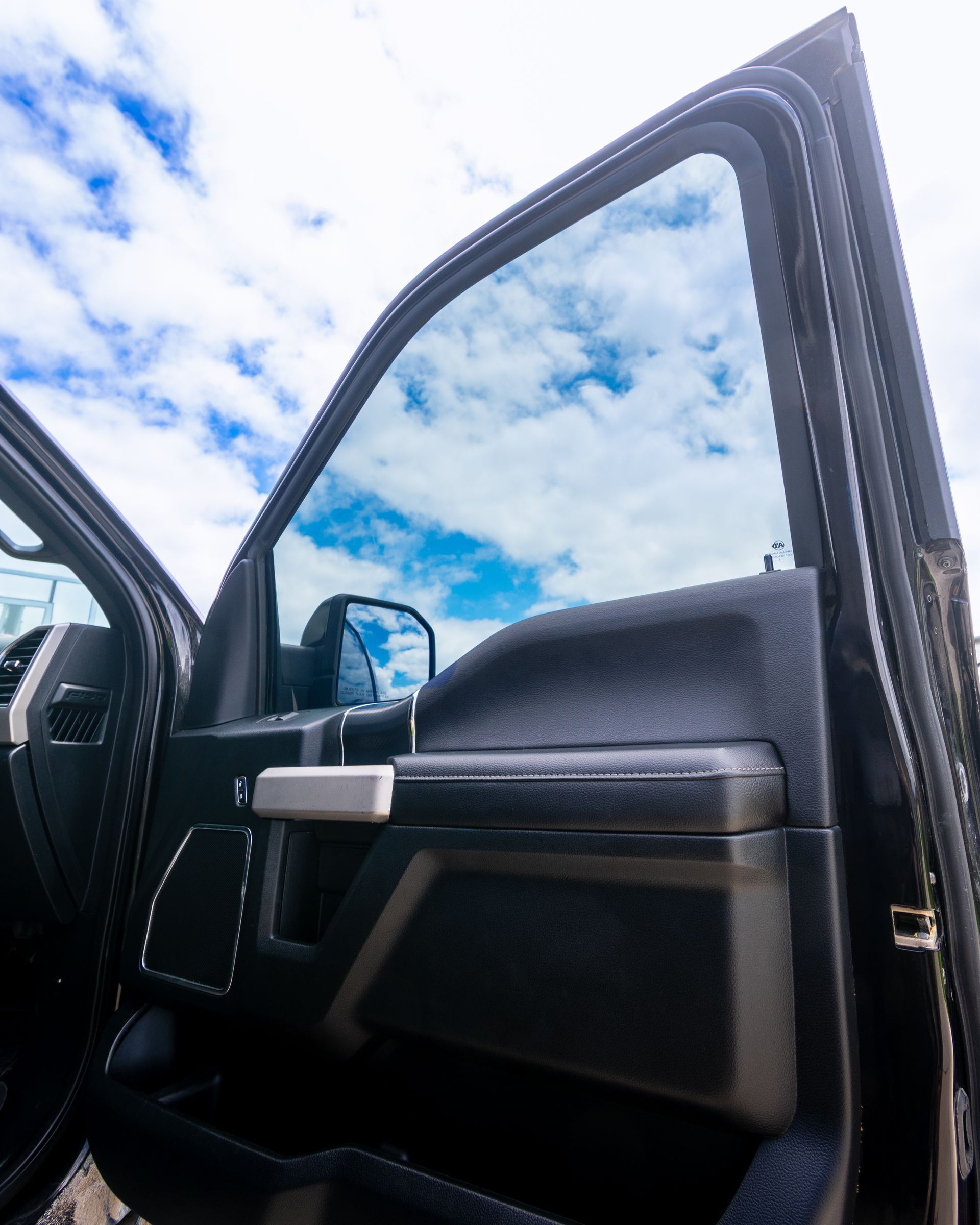 Open car door with black interior against a blue sky