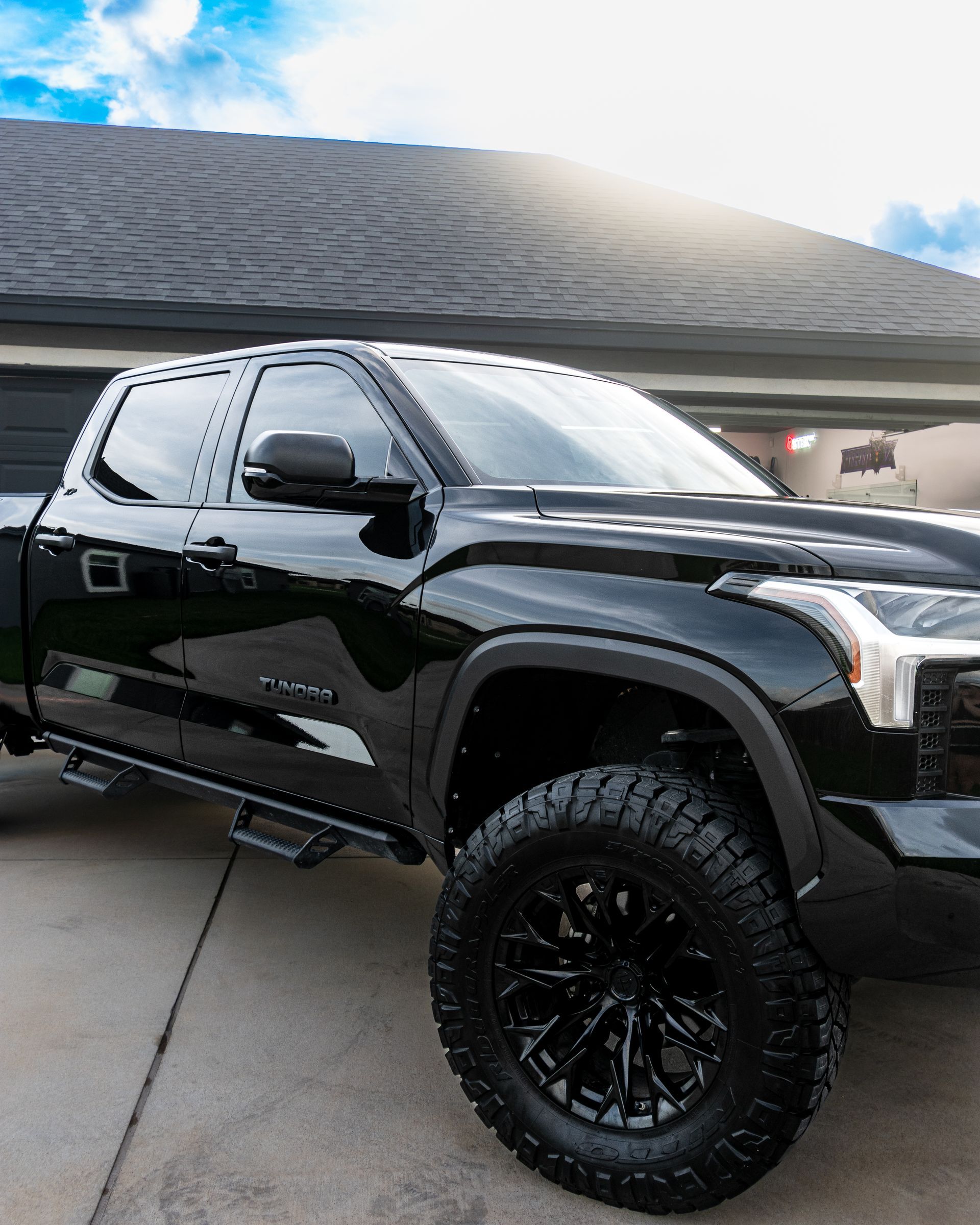 Black lifted pickup truck with large off-road tires parked in a driveway.