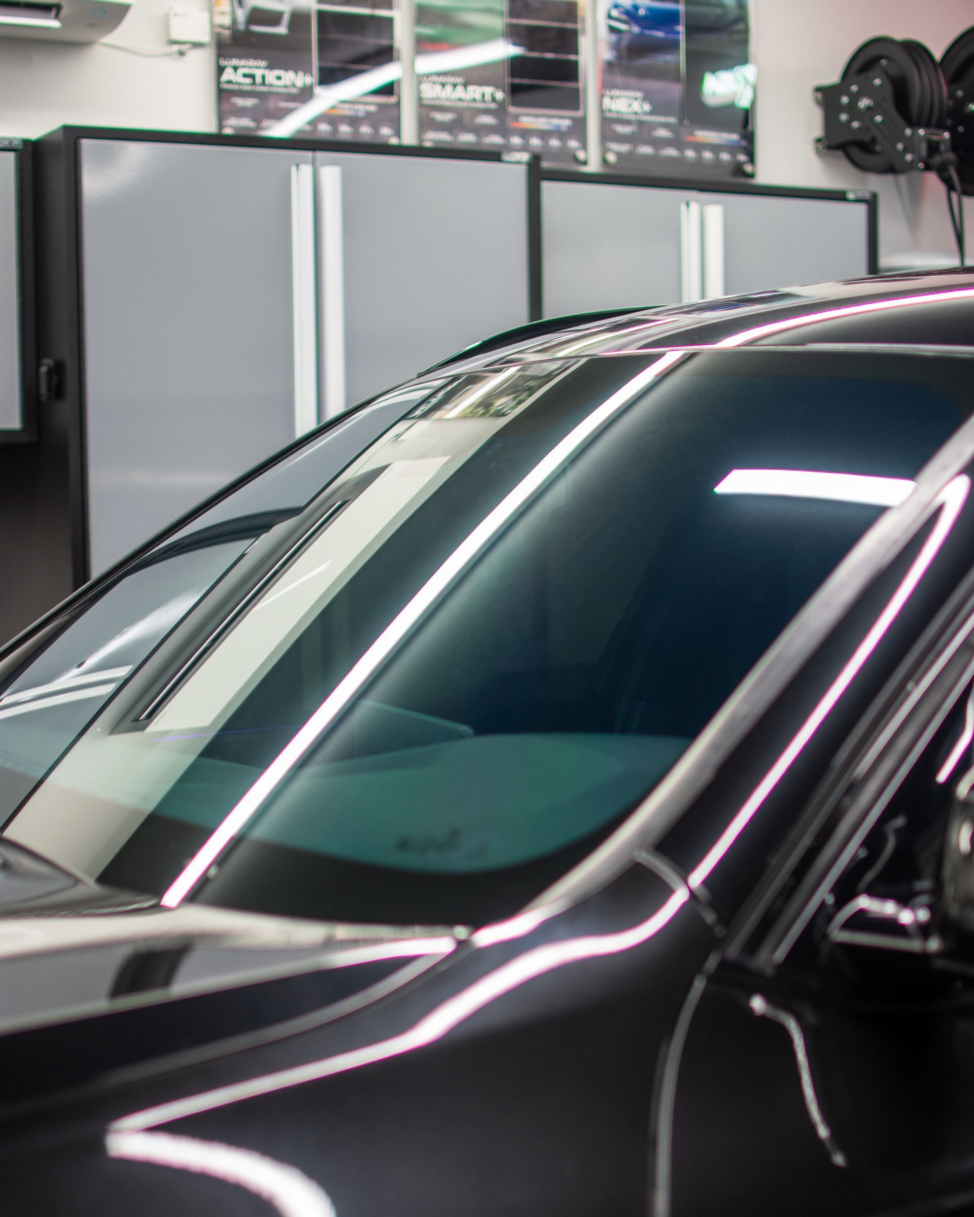 Black-gloved hand wiping a car windshield with a green microfiber cloth