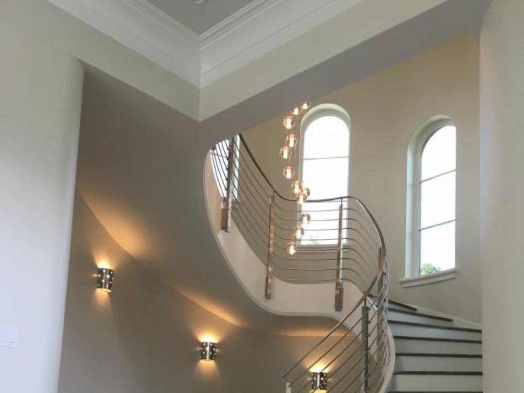 Curved staircase in a bright foyer with white railings and wall sconces.