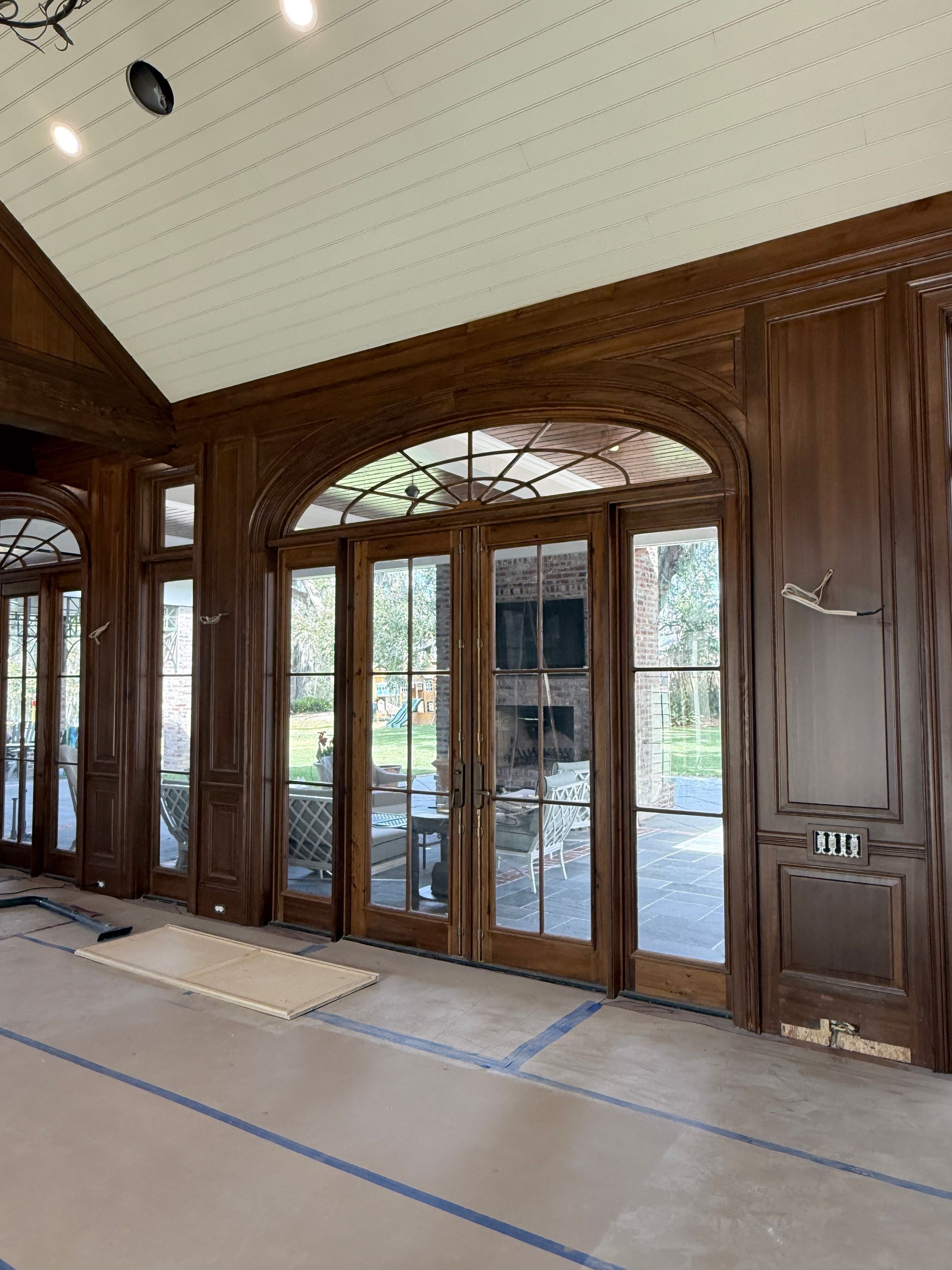 Wood-paneled entry with glass double doors and arched transom, showing a bright outdoor view beyond.